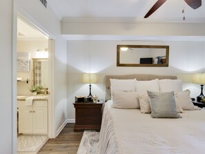 Une chambre à coucher comprenant un lit, des tables de chevet, une commode, un miroir et une porte donnant sur une salle de bain.