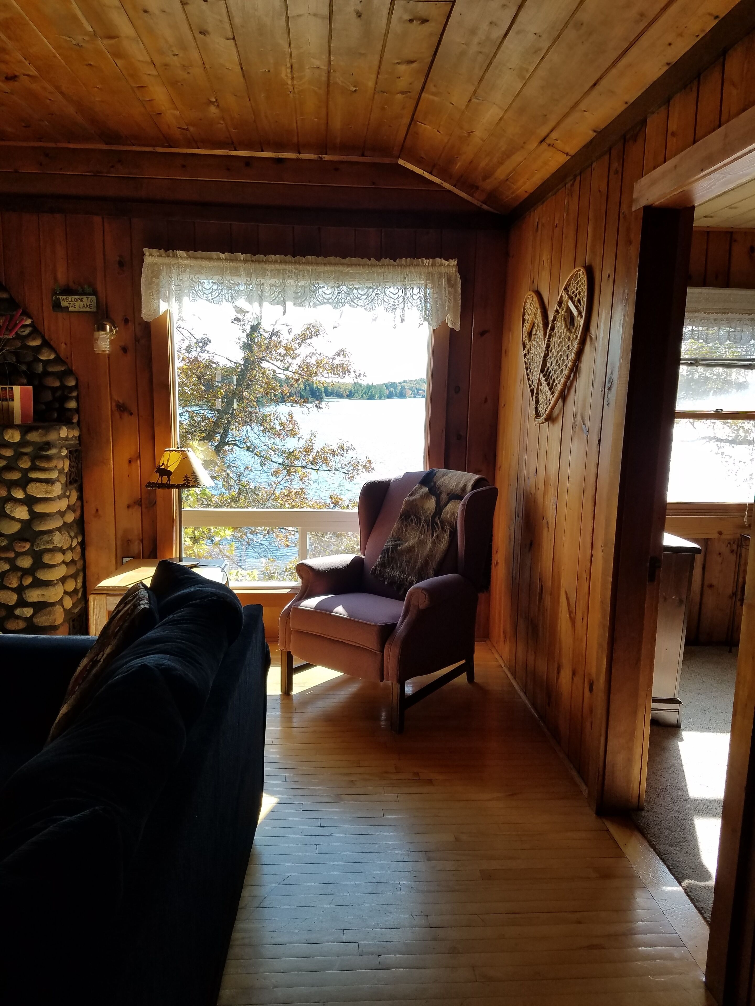 L’intérieur chaleureux d’un chalet avec une cheminée en pierre, un plafond en bois et une vue sur un lac.