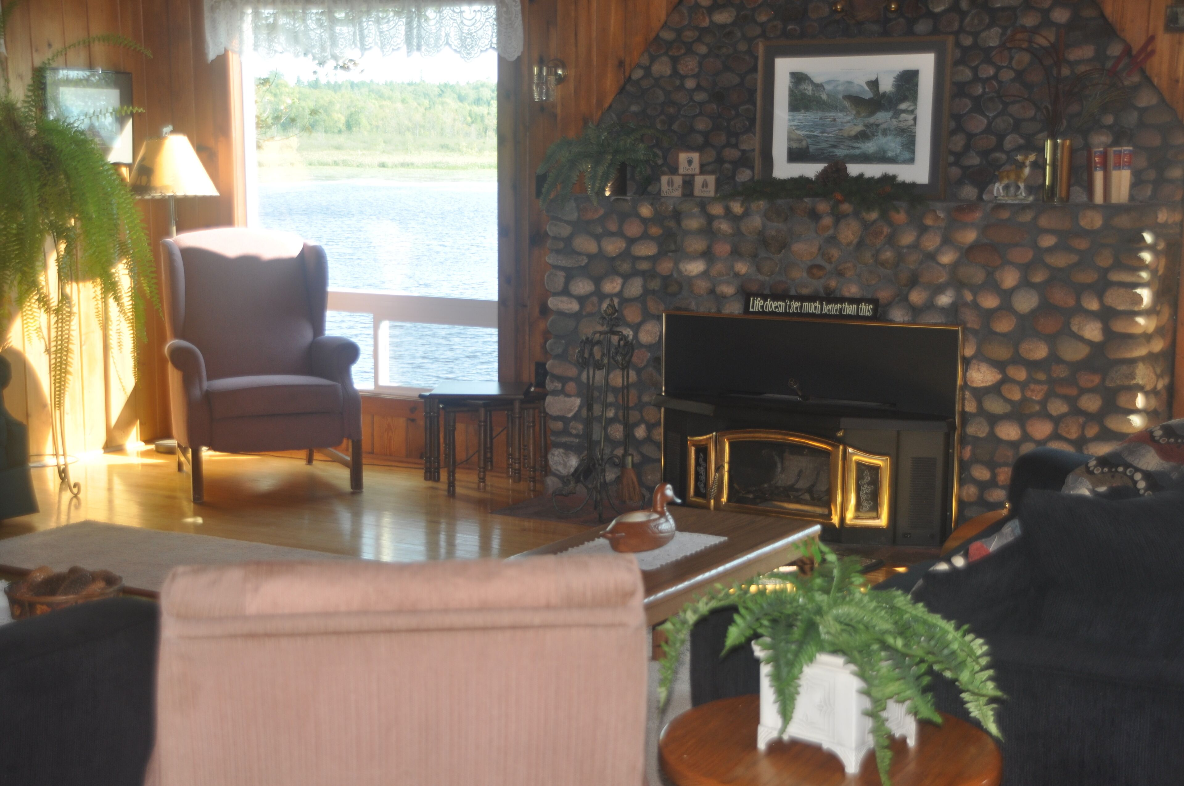 Un salon chaleureux avec une cheminée en pierre, un fauteuil confortable et une vue sur un lac.