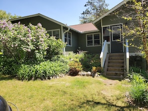 Stroll up the wooden staircase to the front door of this charming two-story home, surrounded by lush greenery and vibrant flowers.