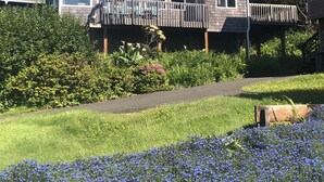 Une maison à deux étages dotée d’une terrasse, entourée d’une végétation luxuriante et agrémentée d’un parterre de fleurs.