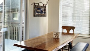 Un coin repas avec une table en bois, des bancs et une vue à travers une porte vitrée.