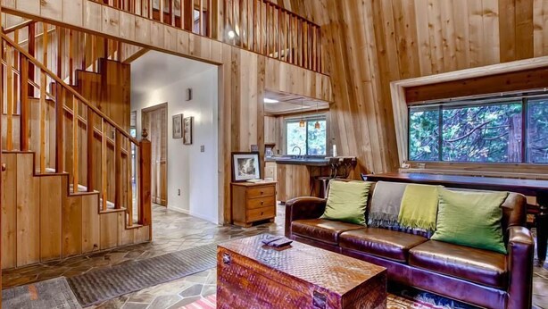 Amplia sala de estar con escalera de madera, sofá de cuero y un gran ventanal con vistas al exterior.