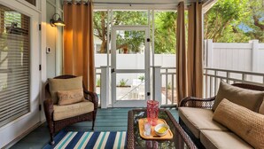 A covered porch with wicker furniture, a glass table with a tray, and a view of a backyard. - Summer Wind: Poolside Retreat Near the Beach & Village (St. Simons Island)
