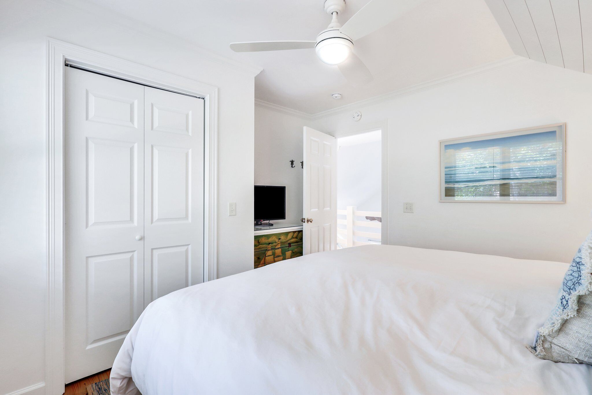 Une chambre à coucher avec un lit, un ventilateur de plafond, un téléviseur et un tableau accroché au mur.
