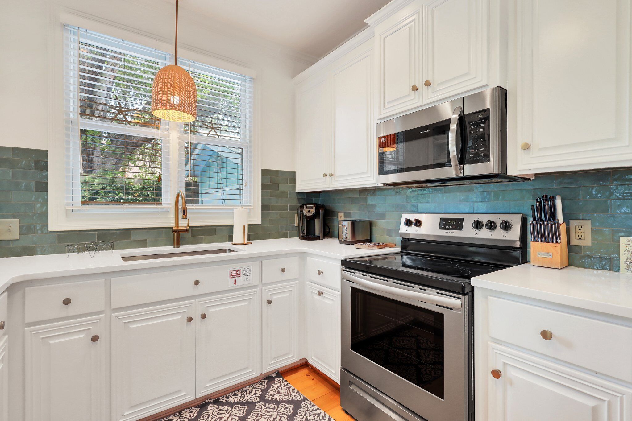 A modern kitchen with white cabinets, stainless steel appliances, and a window with blinds.