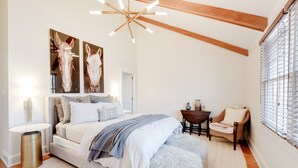 Un dormitorio con cama, una silla, una mesa y obras de arte en la pared.