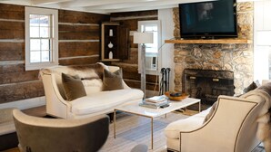 Una sala acogedora con chimenea de piedra, un sofá blanco y un televisor montado encima.