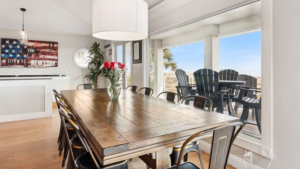 Ein Essbereich mit Holztisch, Stühlen, einer Hängelampe, einem Blumentopf und Blick ins Freie.