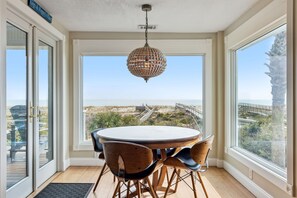 Enjoy meals at the round table surrounded by comfortable chairs, with a view of the beach and a bridge in the distance.