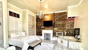 A bedroom with a large bed, a bench, a chandelier, a fireplace, and a bathroom with a bathtub and sink. - Fleur De Lis Mansion ,pool, near French Quarter & Superdome lic.Bnb  317134 (New Orleans)