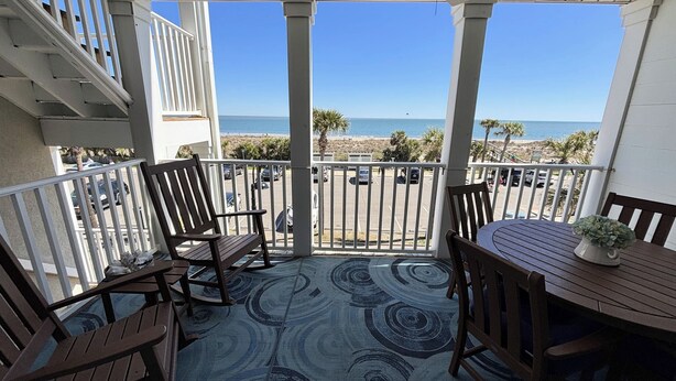 A balcony with a view of the beach, featuring a table and chairs, and a patterned rug. - Beach Front Condo on the Strand, 101 Steps to the Beach  STR2021-00204 (Tybee Island)
