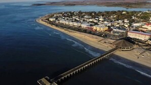 An aerial view of a coastal town with a pier extending into the water, surrounded by residential buildings and a beach. - Beach Front Condo on the Strand, 101 Steps to the Beach  STR2021-00204 (Tybee Island)