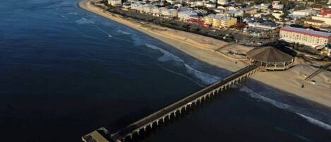 An aerial view of a coastal town with a pier extending into the water, surrounded by residential buildings and a beach.