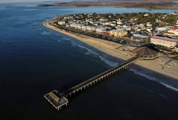 Ein Luftbild einer Küstenstadt mit einem Steg, der sich ins Wasser erstreckt, umgeben von Wohnhäusern und einem Strand.