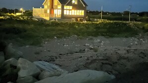 Une maison dotée d’un grand porche et d’une cheminée, entourée d’une zone recouverte de gravier et de quelques plantes.