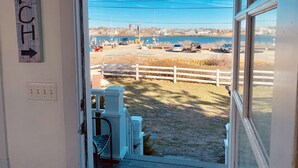 Vue depuis l’intérieur d’un bâtiment, donnant sur une plage, avec une clôture en bois, une jetée et un panneau indiquant la direction de la plage.