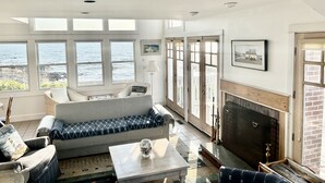 Un salon spacieux doté d’une grande fenêtre donnant sur la mer, d’une cheminée et d’un coin salon confortable.