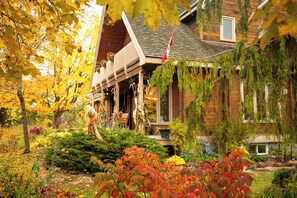 A wooden house with a porch, surrounded by autumn foliage.