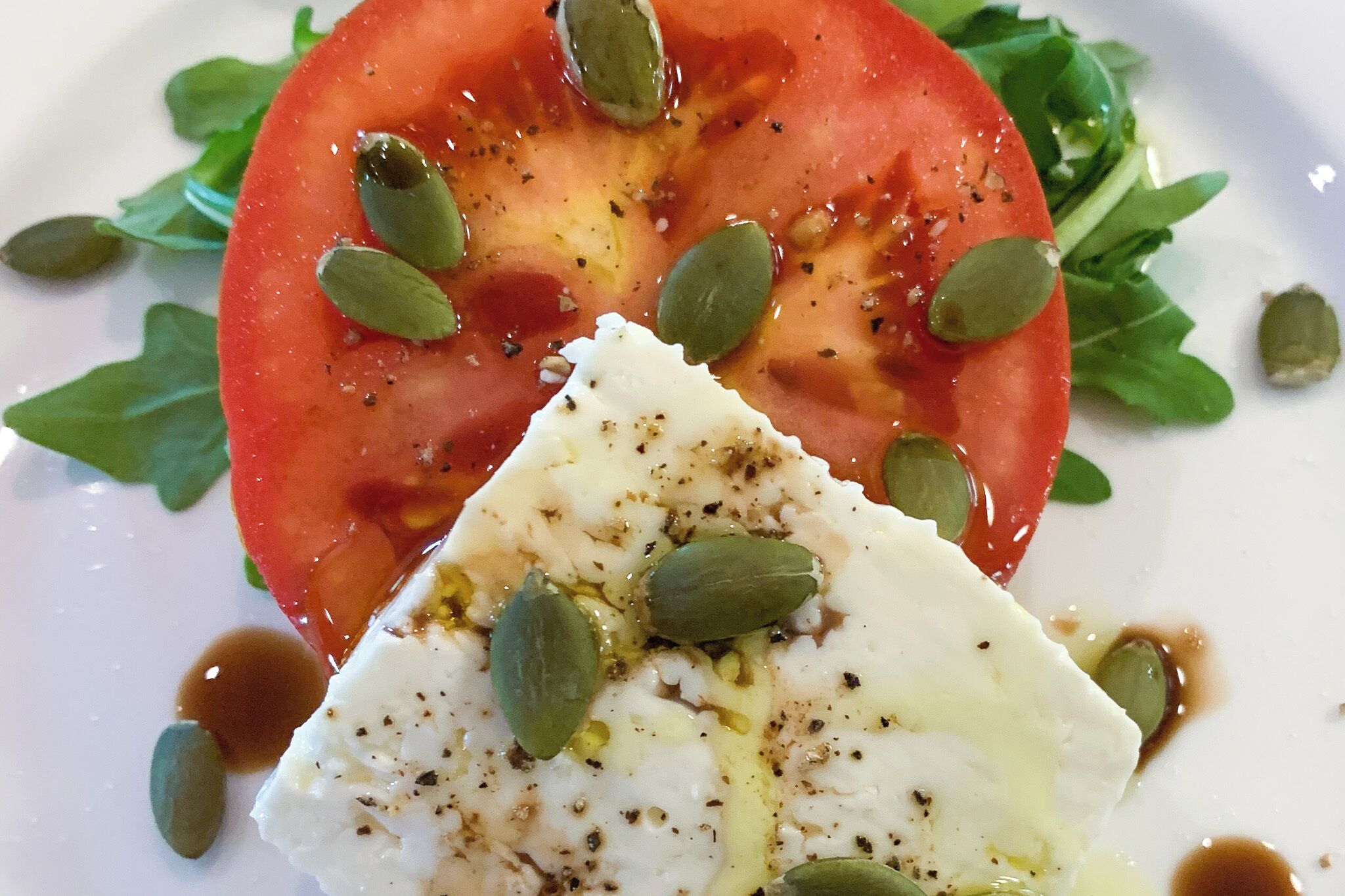 A plate with a slice of tomato, a piece of white cheese, and some green leaves.