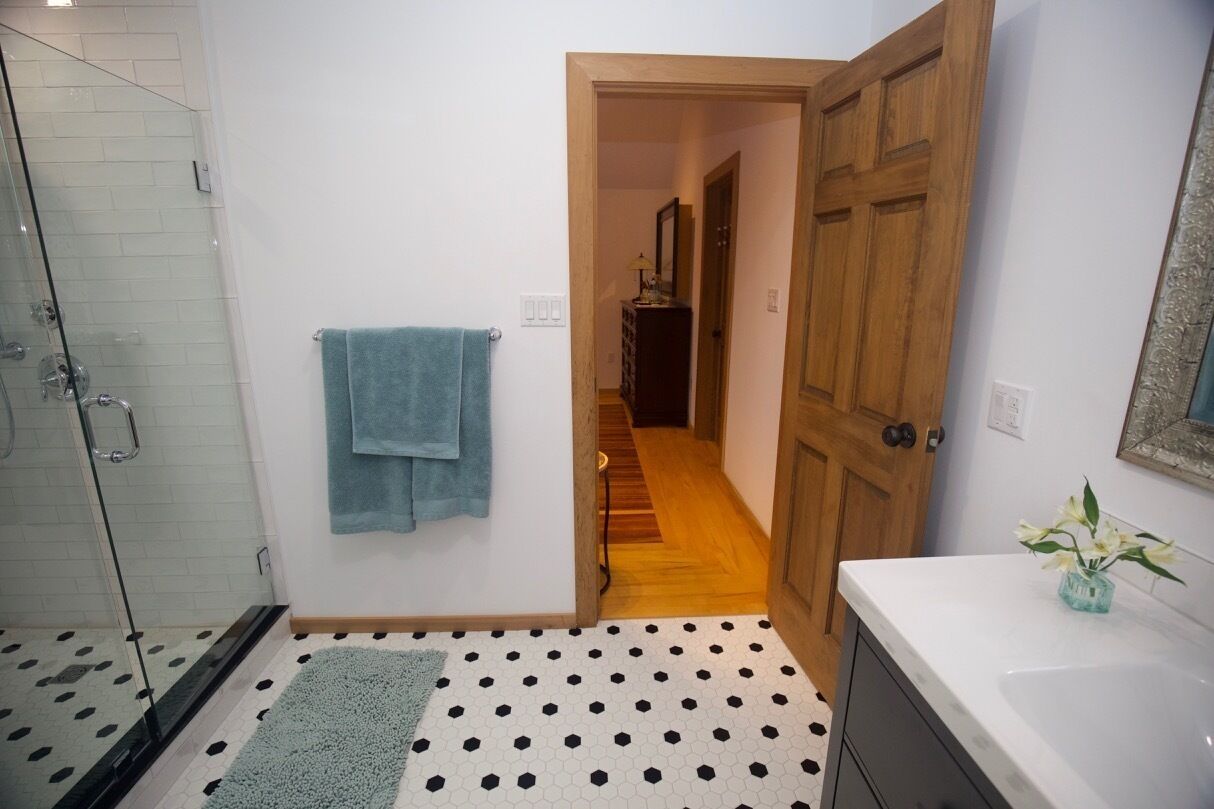 Une salle de bain avec une douche en verre, une serviette bleue, un lavabo blanc et une porte en bois.