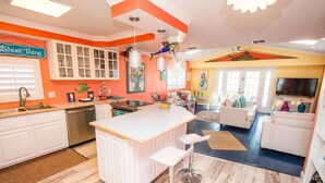 A modern kitchen with white cabinets, a large island, and a dining area with a TV and seating. - A bit of Key West in New Port Richey: Bright Home w/ Pool & Boat Dock Access! (New Port Richey)