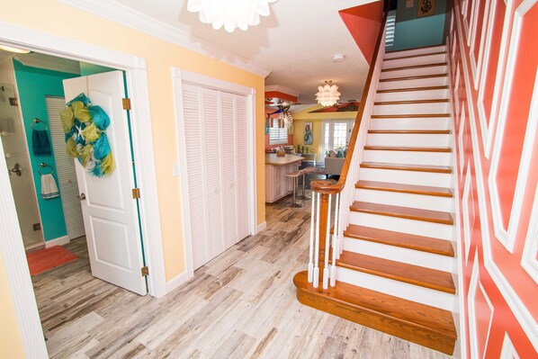 A staircase with wooden steps and white railings, leading to a landing with a kitchen area visible in the background. - A bit of Key West in New Port Richey: Bright Home w/ Pool & Boat Dock Access! (New Port Richey)