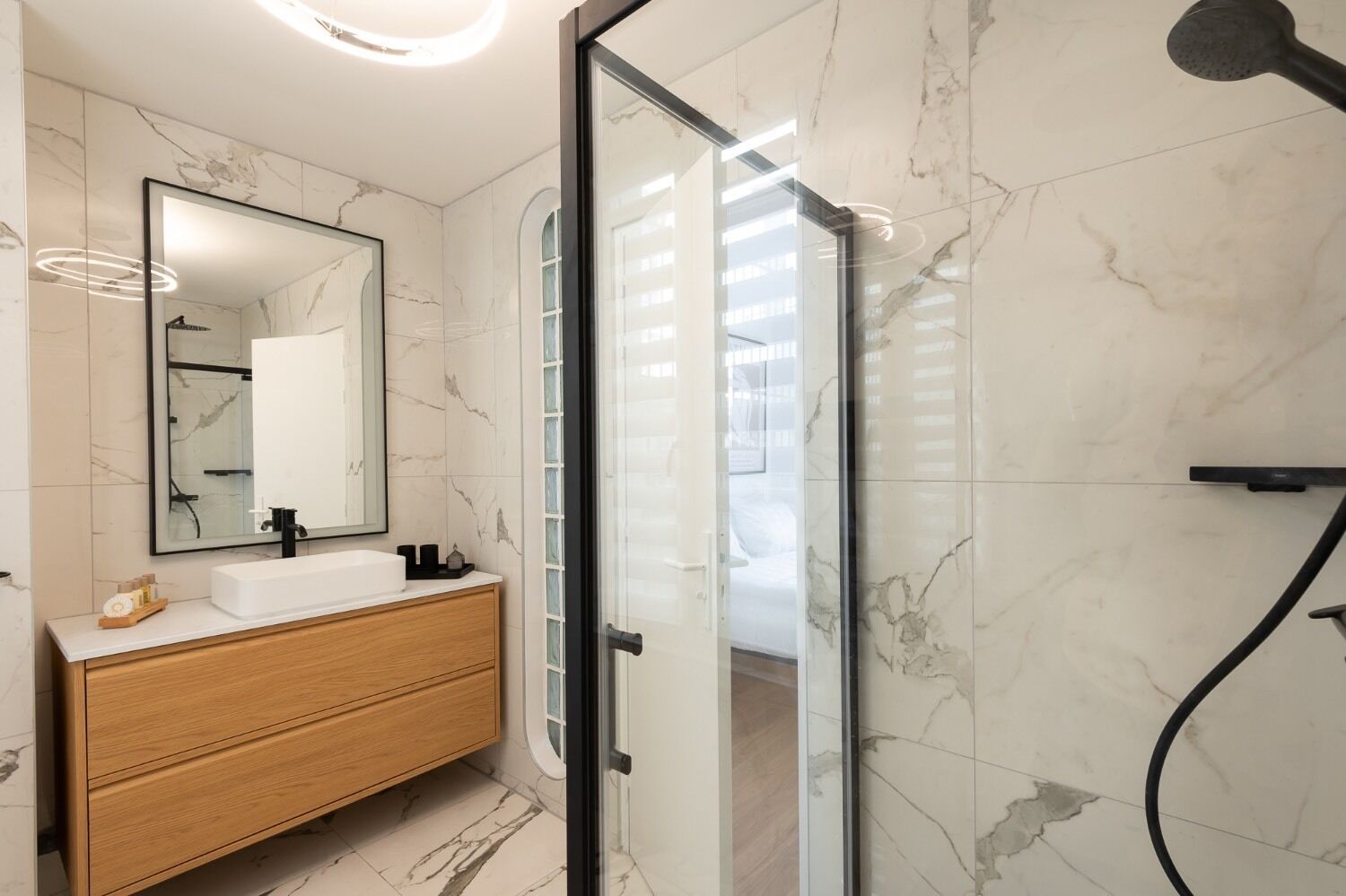 A modern bathroom with a white marble sink, wooden vanity, and a glass shower enclosure.