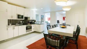 Een moderne keuken met witte kasten, een zwart aanrecht en roestvrijstalen apparatuur. Er is een eethoek met een witte tafel en zwarte stoelen.