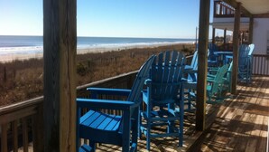 Une terrasse en bois avec des chaises Adirondack bleues donnant sur une plage.