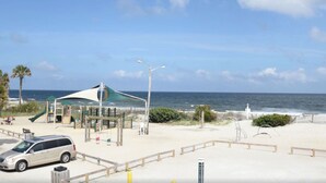 Une vue sur la plage avec une aire de jeux, un espace de repos couvert et une voiture blanche garée sur le sable.