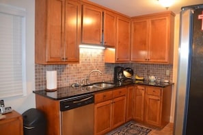 A kitchen with wooden cabinets, a black countertop, a dishwasher, and a tiled backsplash. - Connestee Falls Lakefront Mountain Home  (Brevard)