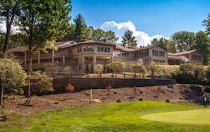 A large, multi-story building with a landscaped front yard and a golf course. - Connestee Falls Lakefront Mountain Home  (Brevard)