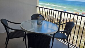A balcony with a round table and four wicker chairs, overlooking a beach with umbrellas and a wooden walkway. - Beachfront - 2 bedrooms for price of one! (Pensacola)