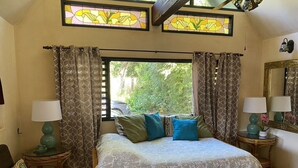 Ein Schlafzimmer mit einem großen Bett, zwei Nachttischlampen, einem Fenster mit Vorhängen, einem Spiegel und einem kleinen Tisch mit einer Lampe.