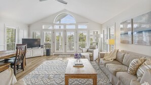 A spacious living room with a high ceiling, large windows, a television, a coffee table, and a sofa.