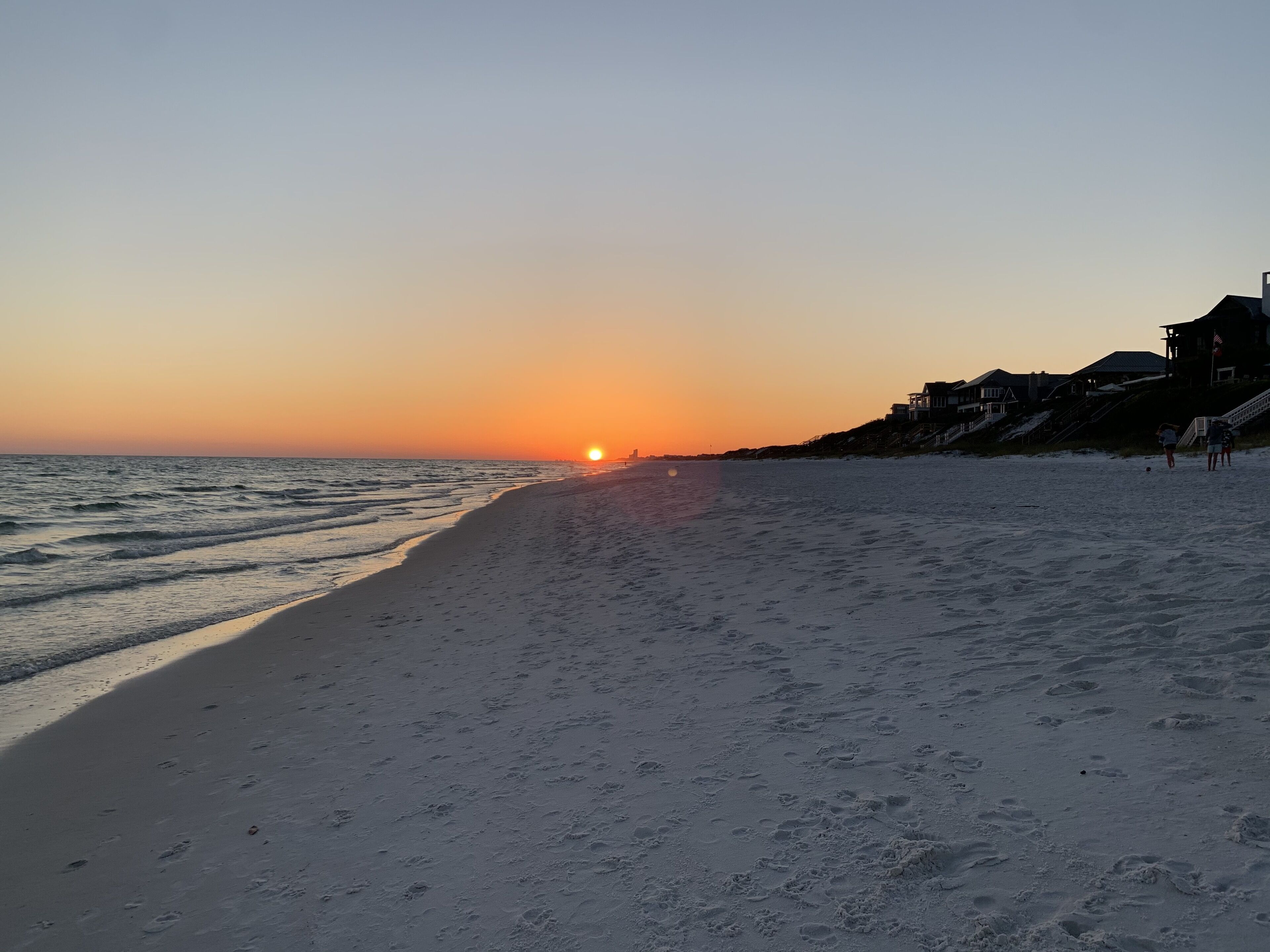 Una playa con un atardecer, orilla arenosa y un edificio a la derecha.