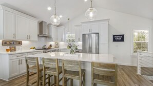 A modern kitchen with white cabinetry, a large island with bar stools, stainless steel appliances, and pendant lighting.