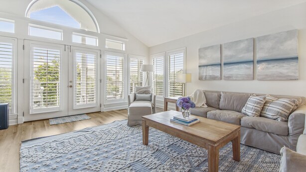 A spacious living room with a large window, a sofa, a coffee table, and a rug.