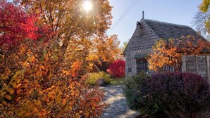 A rustic wooden house with a sloped roof, surrounded by a garden with autumn foliage. - Charming Cottage on Main St. in Historic St. Charles! Jetted Tub, 2 Fireplaces!! (St. Charles)