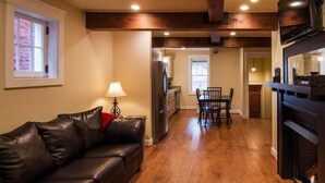 A cozy living room with a leather sofa, a dining table with chairs, a kitchen area with a refrigerator, and a fireplace. - Charming Cottage on Main St. in Historic St. Charles! Jetted Tub, 2 Fireplaces!! (St. Charles)
