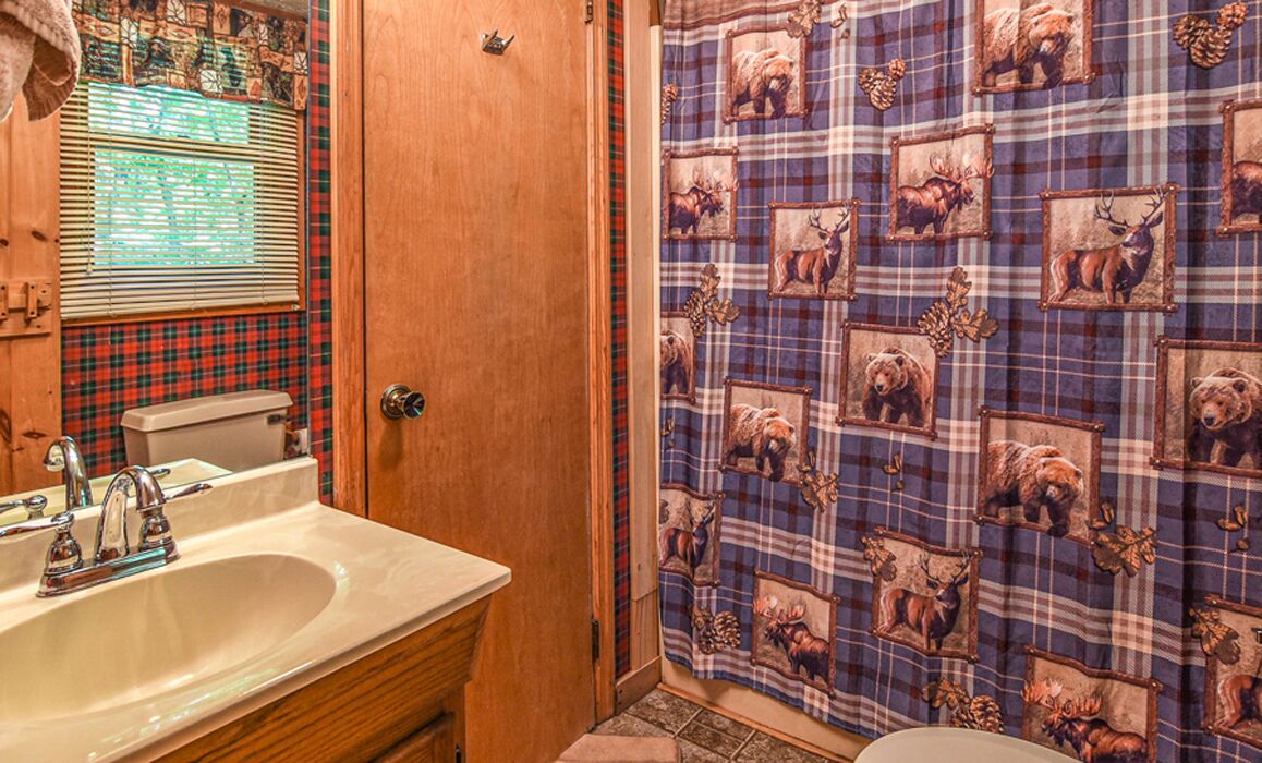 A bathroom with a wooden door, a sink with a mirror, and a shower curtain with a plaid pattern.