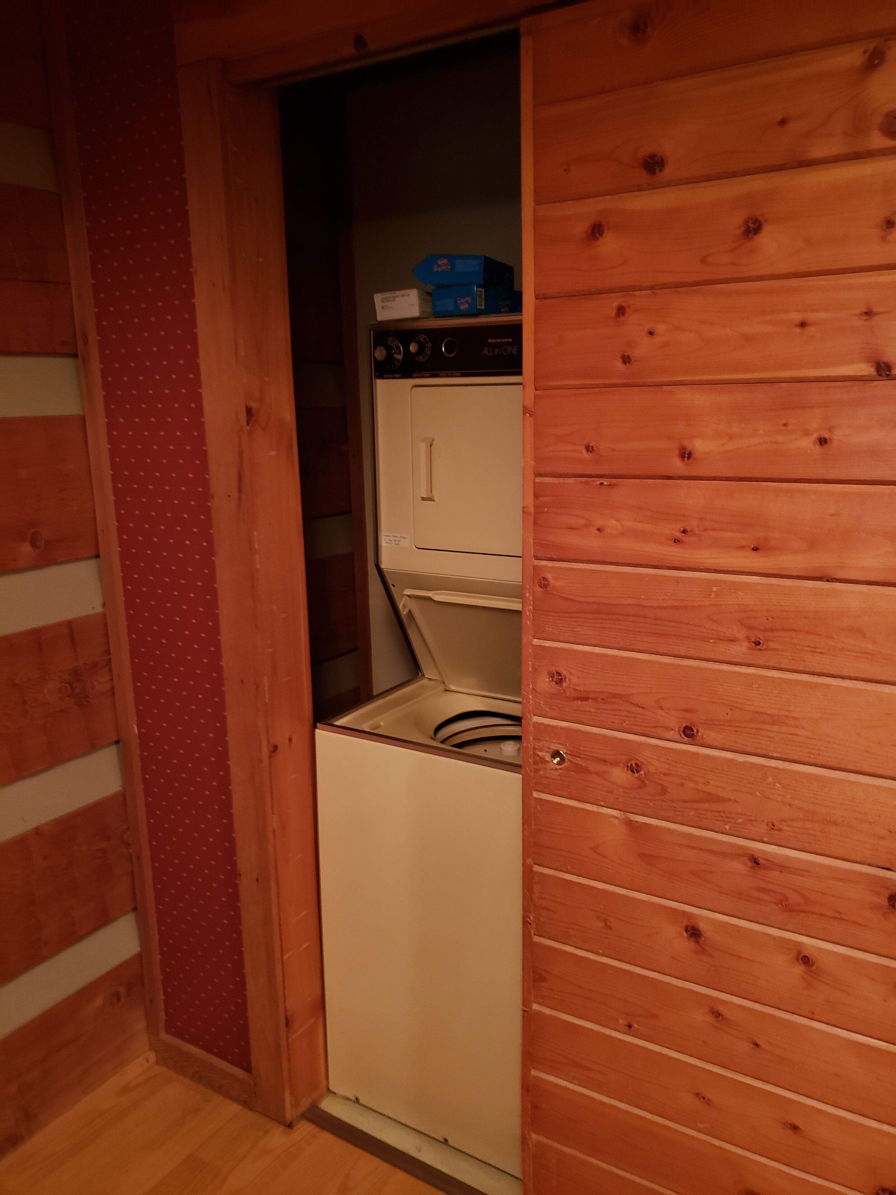 A compact, wooden-walled laundry room with a front-loading washing machine and dryer.