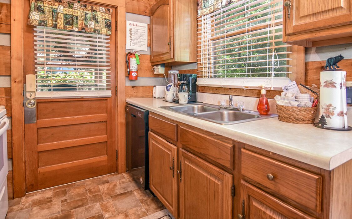 Una cocina con armarios de madera, un fregadero de acero inoxidable y una ventana con persianas.