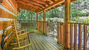 Une terrasse en bois avec un fauteuil à bascule et un banc, entourée d’une balustrade en bois, donnant sur une zone boisée.