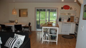 A modern kitchen with a dining area, a black sofa with decorative pillows, and a view through the glass door. - 4 Bed 2 Bath Escape in the Woods. 10 minutes to the beach! (La Pointe)