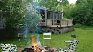 A backyard with a fire pit, two chairs, and a deck overlooking a grassy area. - 4 Bed 2 Bath Escape in the Woods. 10 minutes to the beach! (La Pointe)
