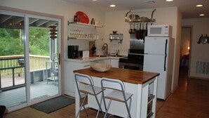 A modern kitchen with a wooden island, bar stools, a refrigerator, and a view of the outdoors. - 4 Bed 2 Bath Escape in the Woods. 10 minutes to the beach! (La Pointe)