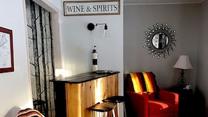 A living room with a red armchair, a wooden cabinet, a wall-mounted sign reading "WINE & SPIRITS", and a decorative mirror. - 4 Bed 2 Bath Escape in the Woods. 10 minutes to the beach! (La Pointe)