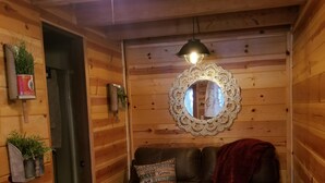 Un acogedor interior de cabaña con detalles de madera, un sofá de cuero, una mesita, un espejo y un ventilador de techo.